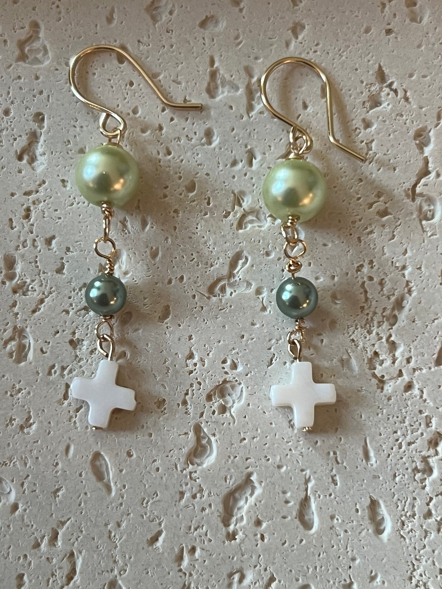 Flat lay with light green pearl beads, small teal pearl accents, and white cross pendants on gold hooks