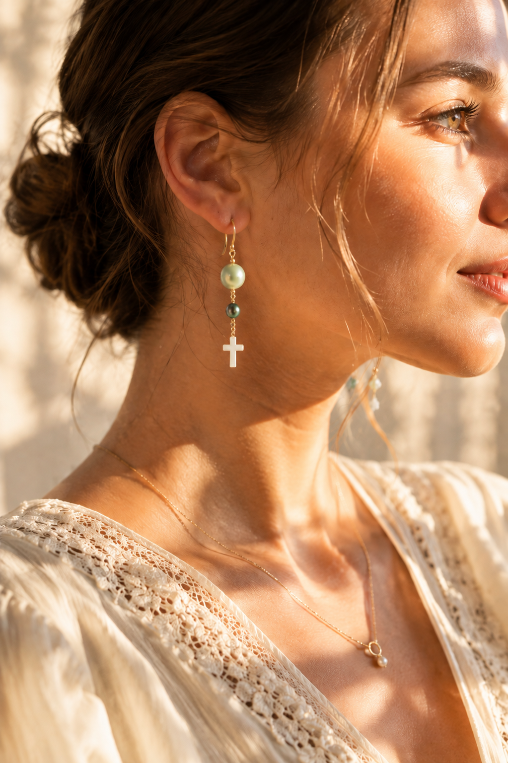 Close-up of woman wearing earrings with green and gray pearl beads and white cross drop in sunlight