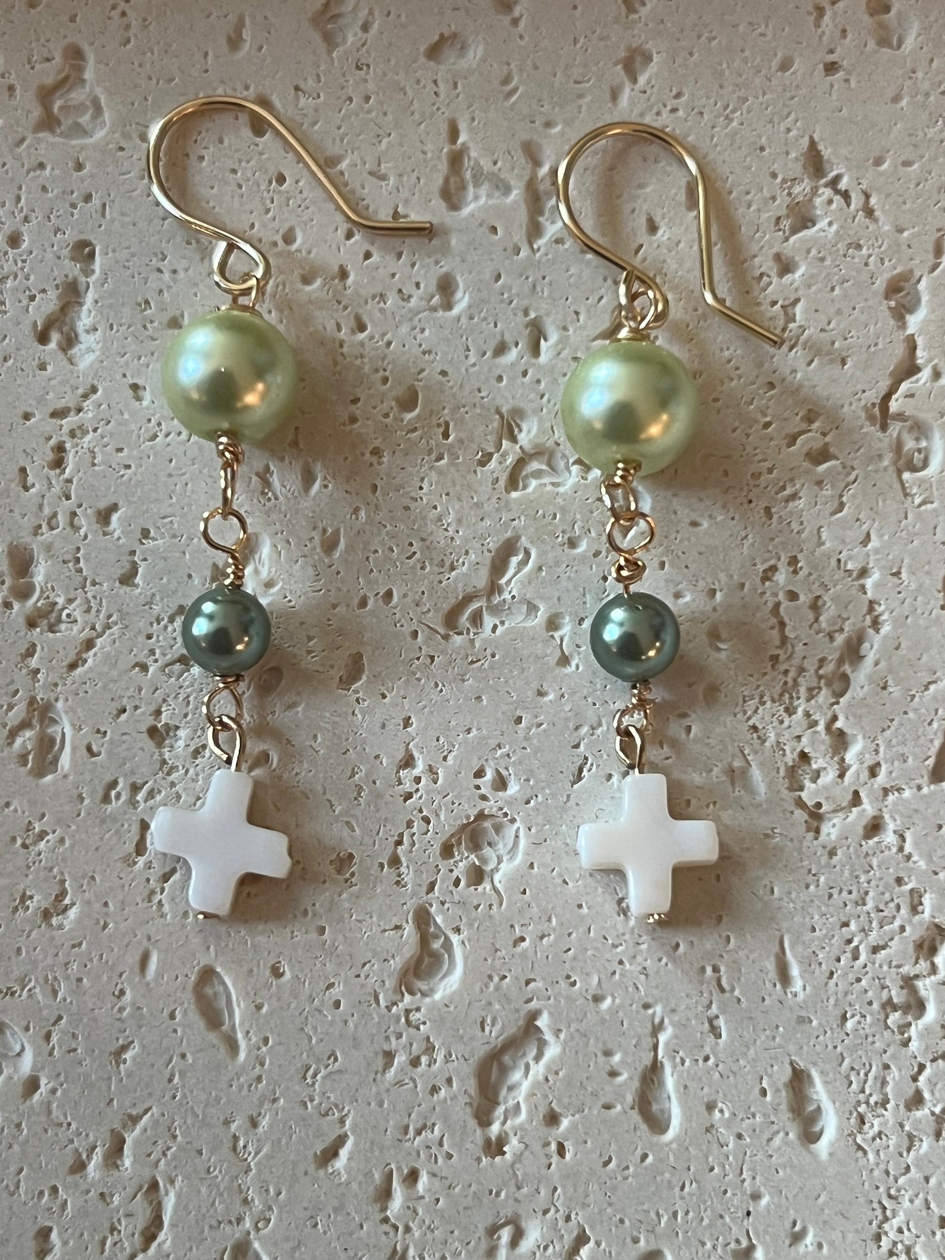 Flat lay with light green pearl beads, small teal pearl accents, and white cross pendants on gold hooks