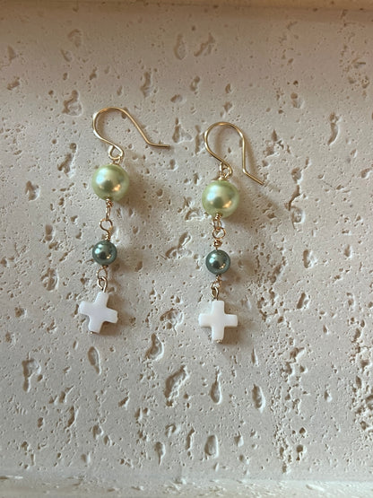 Pair laid flat showing light green pearl tops, teal pearl beads, and white cross drops on gold hooks

